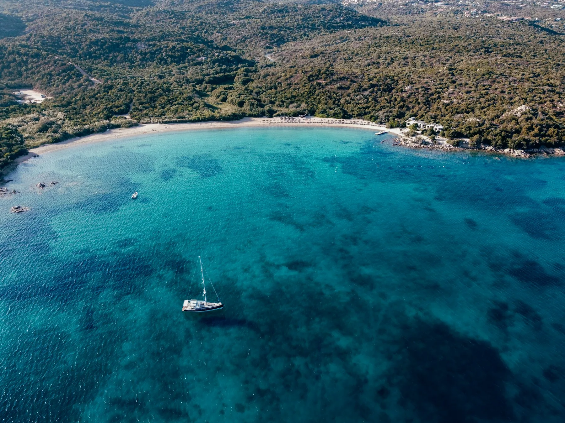 A quiet Mediterranean bay with a sailing boat and wooded coastline