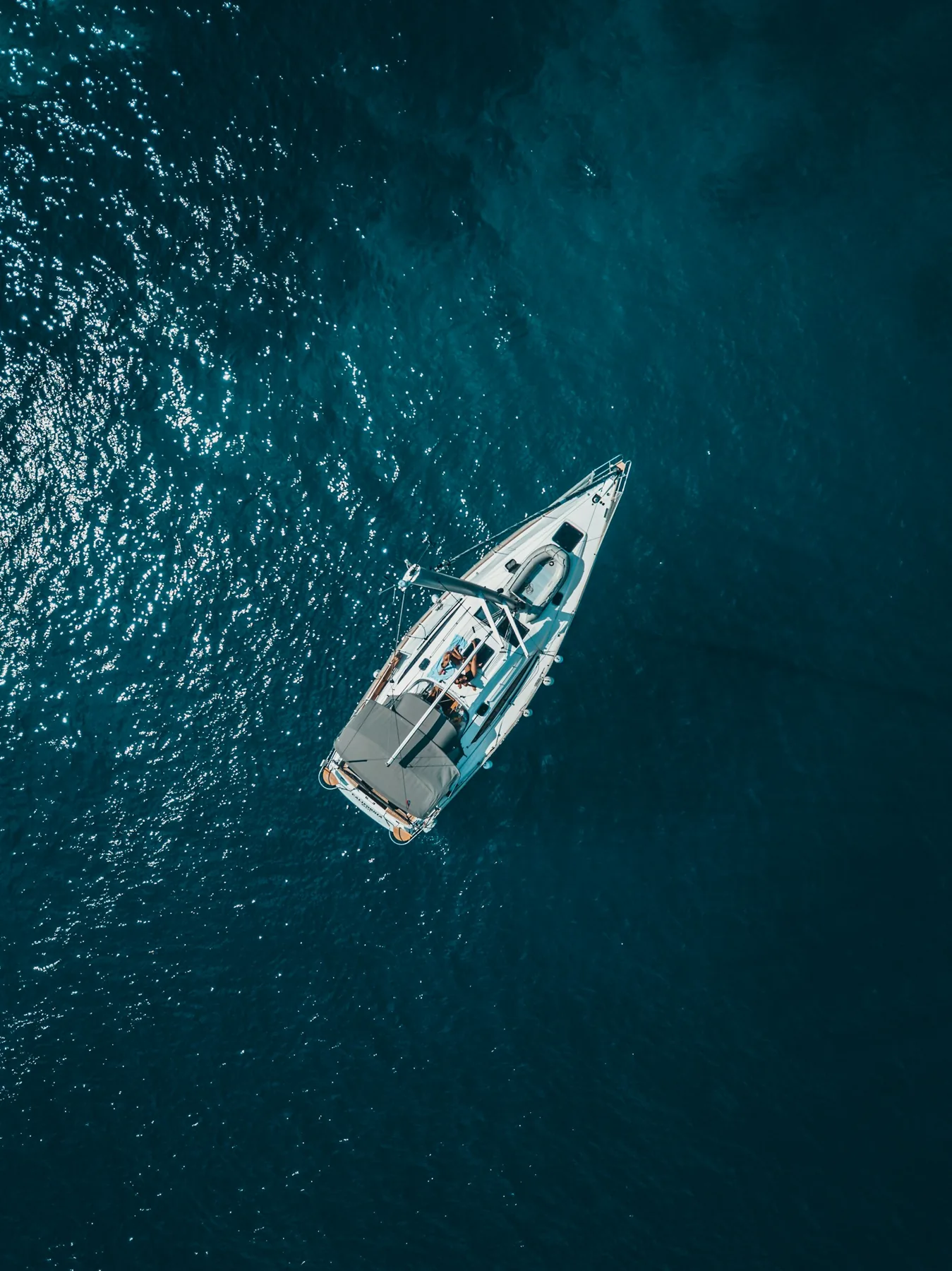 A sailing boat seen from above in deep blue coastal water